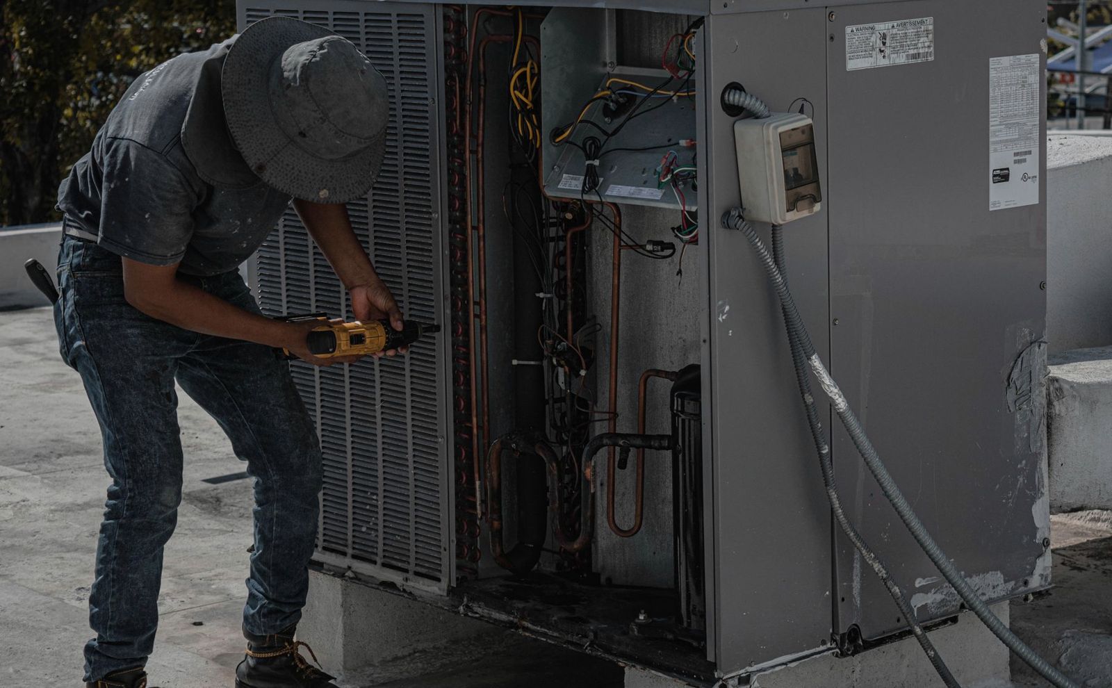 Technician with a cordless drill opening the panel of an outdoor air conditioning unit